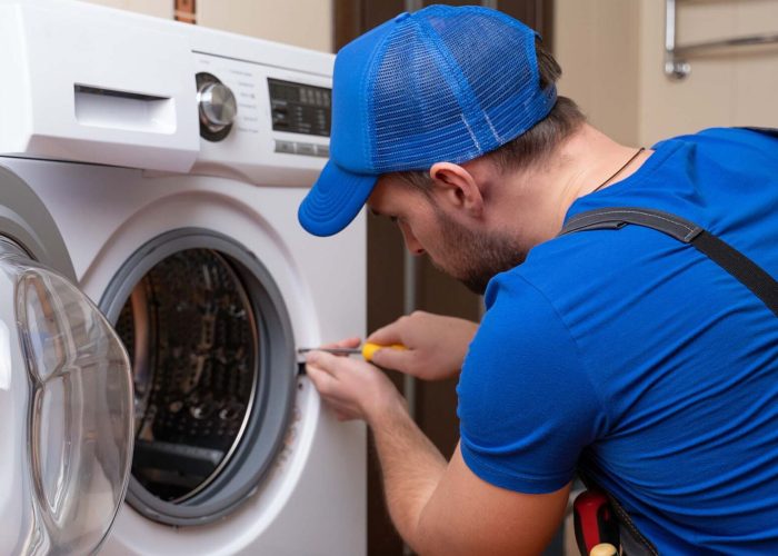 Working man plumber repairs a washing machine in home. Washing machine installation or repair. plumber connecting appliance.